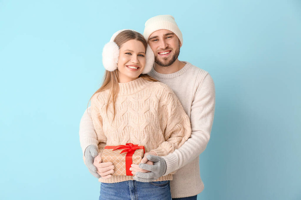 Portrait of happy couple in winter clothes and with gift on color background - Photo, Image