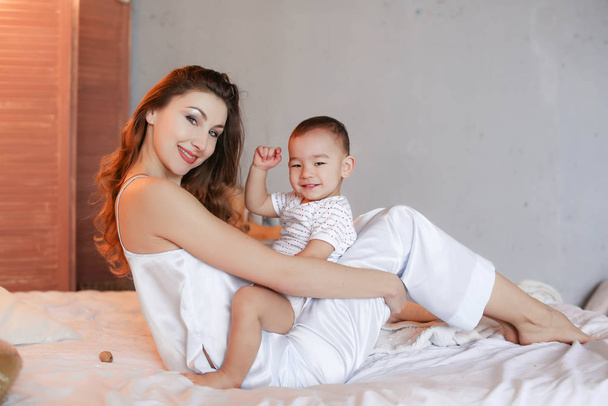 Maman et bébé s'amusent et s'amusent tôt le matin dans la chambre sur le lit
 - Photo, image