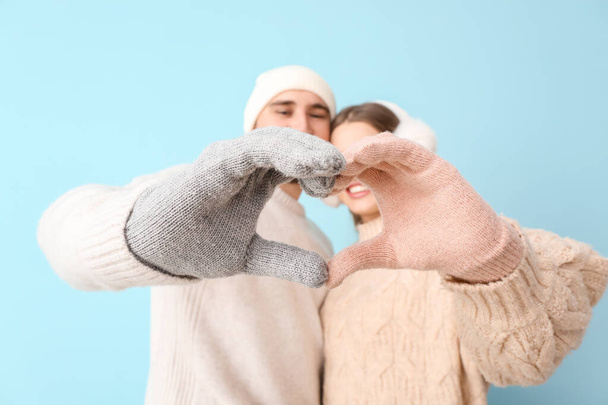 Happy couple in winter clothes making heart shape with their hands on color background - Photo, Image