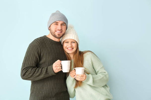 Portrait of happy couple in winter clothes and with cups of hot tea on color background - Photo, image