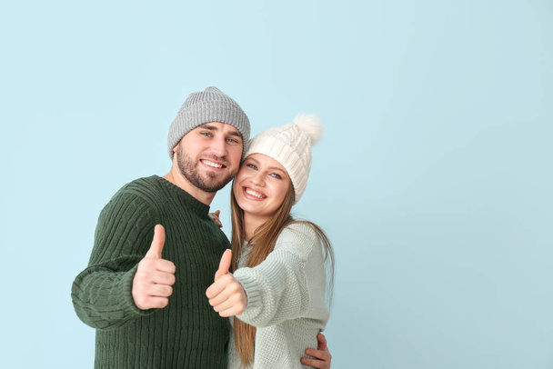 Portrait of happy couple in winter clothes showing thumb-up gesture on color background - Fotoğraf, Görsel