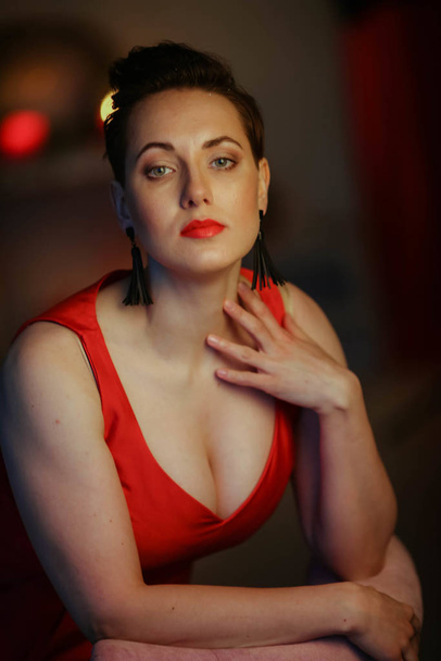 Close-up of a plump woman in a red dress on the background of a glowing blurred Christmas tree - Fotoğraf, Görsel