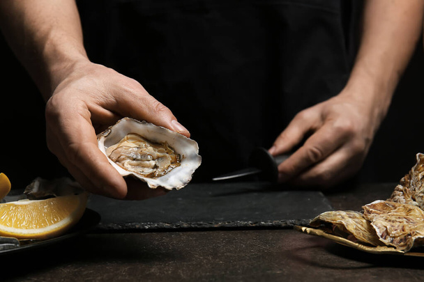 Man opening shell of fresh oyster on dark background - Foto, Imagem