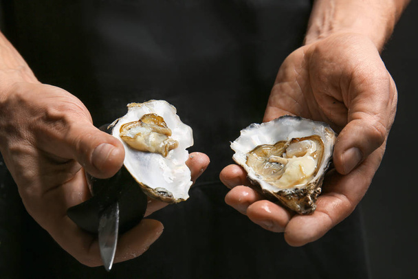 Mann öffnet Schale frischer Austern auf dunklem Hintergrund - Foto, Bild
