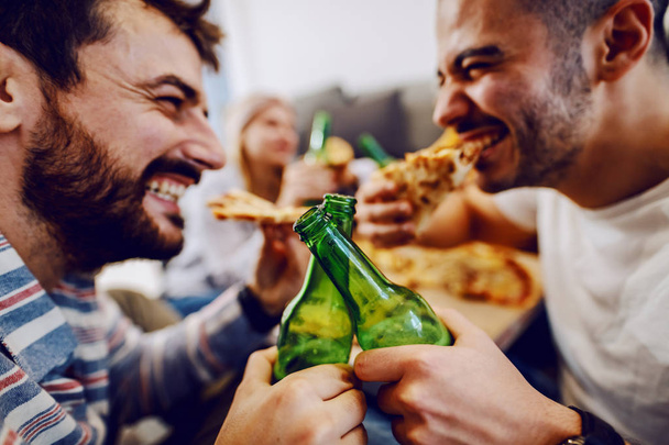 Bir grup arkadaş oturma odasında yerde oturuyor, bira içiyor ve pizza yiyorlar. Ev partisi. - Fotoğraf, Görsel