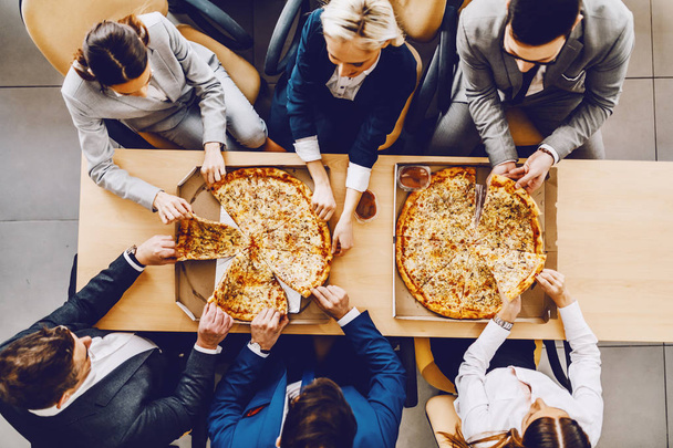 Верхний вид голодных коллег, сидящих за столом и обедающих пиццей. Корпоративный интерьер
. - Фото, изображение