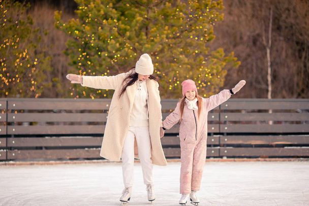kleines entzückendes Mädchen mit ihrer Mutter beim Schlittschuhlaufen auf der Eisbahn - Foto, Bild