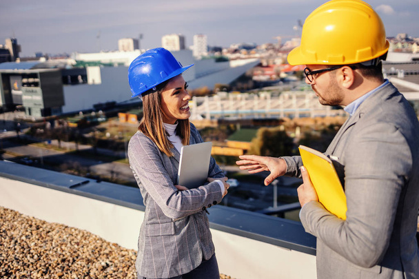 Handsome real estate seller talking to a female investor and convinces her to buy building. They are standing on top of building. - Photo, Image