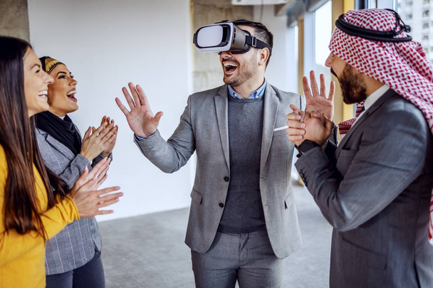 Real estate agent having vr goggles and having virtual presentation of building he standing in. Around him arab investors and his colleague clapping. - Photo, image