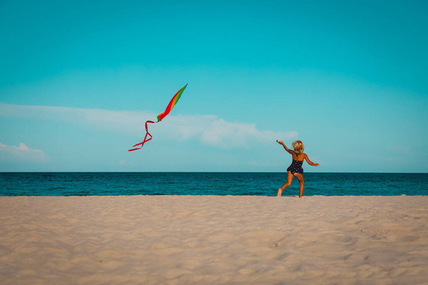 Happy cute little girl flying a kite on beach - Fotó, kép