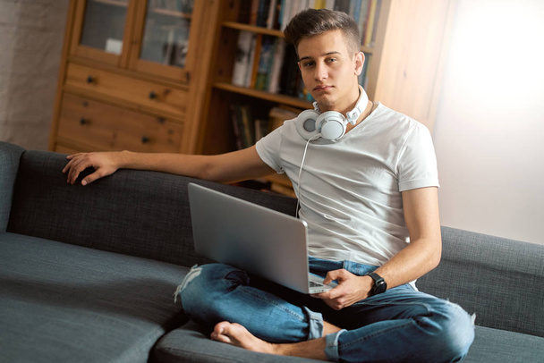 Молодой красивый мужчина с ноутбуком на сером диване дома
  - Фото, изображение