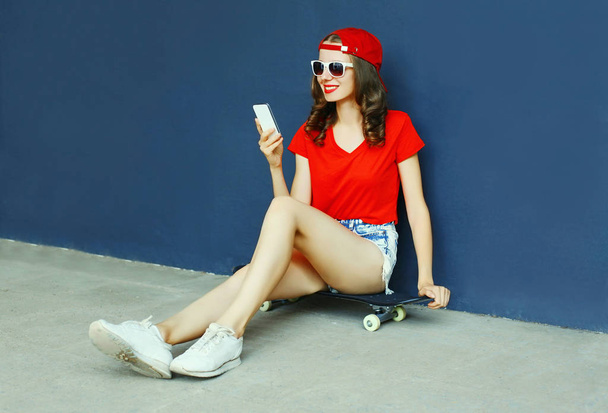 Onnellinen hymyilevä nuori nainen puhelimen kanssa istuu rullalauta weari
 - Valokuva, kuva