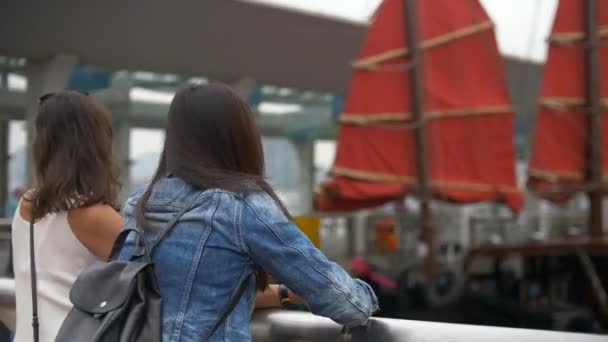 Dos mujeres guapas jóvenes miran el barco con velas rojas y ríen 4k
 - Metraje, vídeo