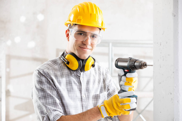 Young construction worker drilling wall indoors - Foto, Imagem