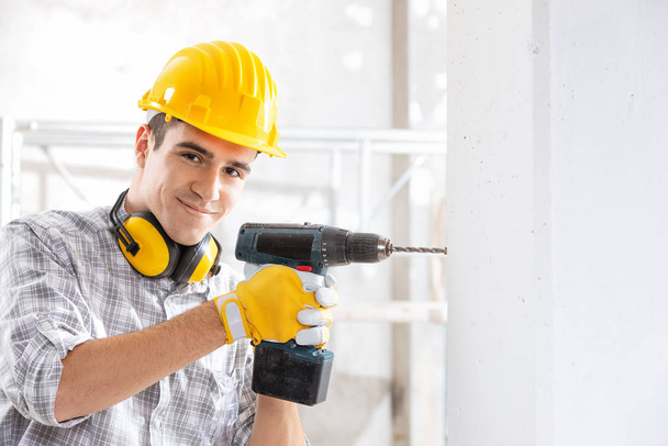 Young construction worker drilling wall indoors - Valokuva, kuva