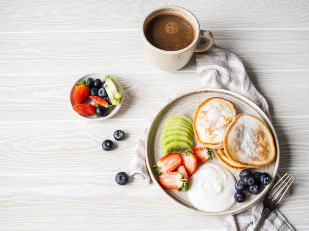 Νόστιμο πρωινό - τηγανίτες, πασπαλισμένες με άχνη ζάχαρη με φρούτα και μούρα - Φωτογραφία, εικόνα