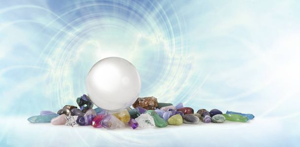 Magische Healing Crystal Vortex Achtergrond - een grote heldere kristallen bol bovenop een selectie van helende kristallen stenen tegen een lichtblauwe spiraalvormige vortex met kopieerruimte - Foto, afbeelding
