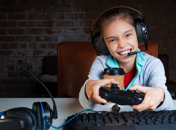 Une jeune fille est assise devant un moniteur et joue à des jeux vidéo avec un visage heureux et excité
. - Photo, image