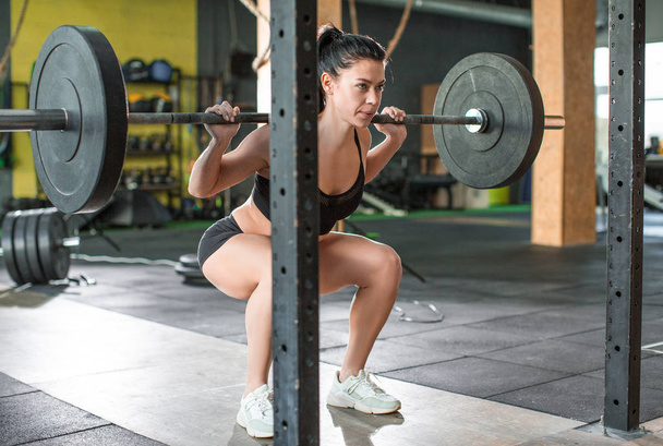Foto van een vrouw is het heffen van gewicht tijdens het sporten met lange halter in de sportschool. - Foto, afbeelding