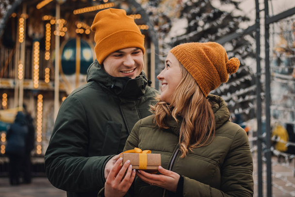 Man gives a small present with a yellow ribbon to his girlfriend on the street. Woman takes a gift from her boyfriend. Valentines day concept. - Photo, Image
