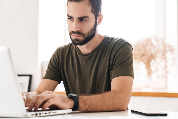 Image of caucasian thinking man typing on laptop while sitting - Фото, изображение