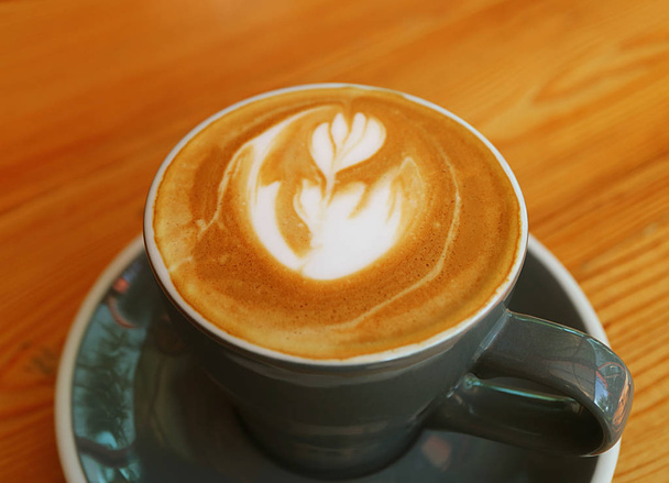 Café Cappuccino quente com arte Latte em uma xícara cinza escuro servido na mesa de madeira
 - Foto, Imagem