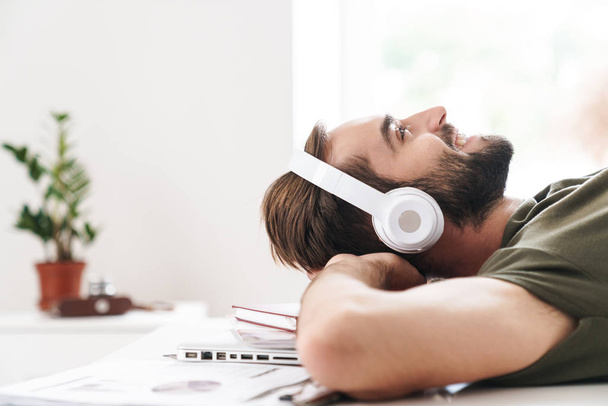 Image of man listening music with headphones while lying on desk - Fotó, kép