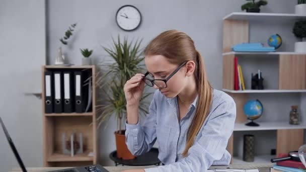 Tired from her working on laptop young pleasant blond lady taking off her glasses and rubbing her eyes - Imágenes, Vídeo