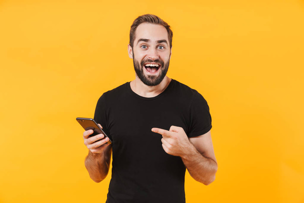 Image of surprised man wearing t-shirt smiling and holding smart - Fotoğraf, Görsel