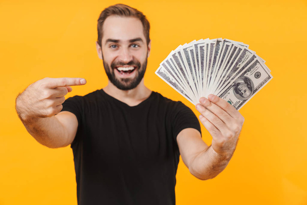 Image of positive man wearing t-shirt smiling and holding money  - 写真・画像