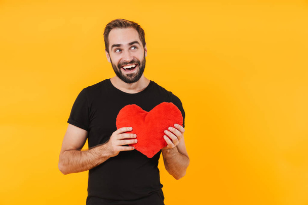 Image of romantic man wearing t-shirt smiling and holding red pa - Фото, изображение