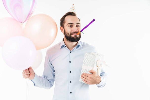Image of man blowing party horn while holding air balloons and p - Foto, afbeelding
