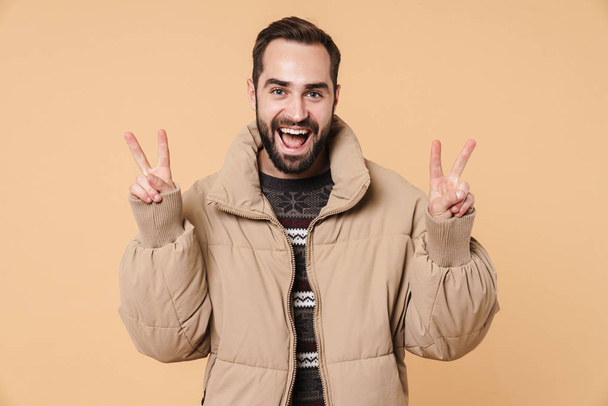 Image of happy man wearing winter jacket smiling and showing pea - Φωτογραφία, εικόνα