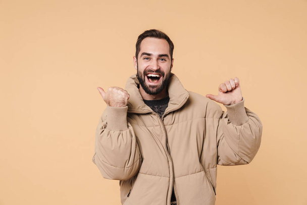 Image of young man in winter jacket smiling and pointing fingers - Foto, imagen