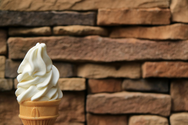 Widok z przodu Milky White Vanilla Soft Serve Ice Cream stożek z niewyraźne ciemnobrązowe bloki kamienne Ściana w tle - Zdjęcie, obraz