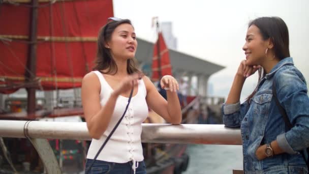 attraktive junge Frau spricht mit Freundin, die mit rotem Segelboot hinter ihr winkt - Filmmaterial, Video