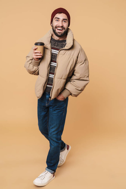 Image of man in winter jacket and hat smiling while holding coff - Foto, Bild