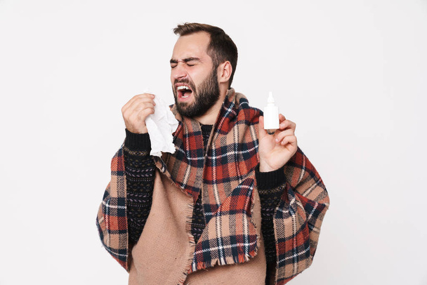 Portrait of ill guy wrapped in blanket sneezing and holding nose - Photo, Image