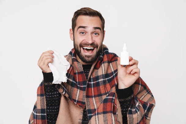 Portrait of ill guy wrapped in blanket sneezing and holding nose - Valokuva, kuva