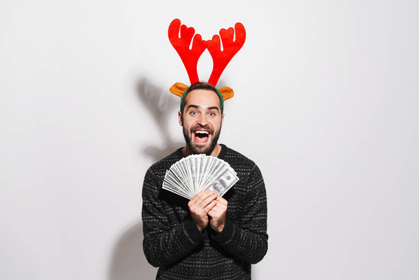 Image of man in Christmas reindeer antlers holding dollar bankno - Foto, Imagen