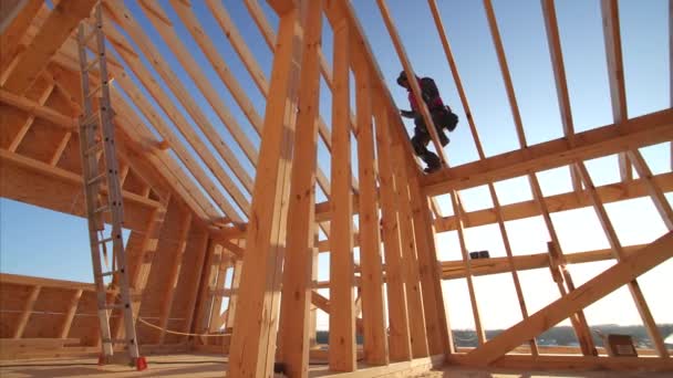 builders working at unfinished frame house interior with wooden beams of roof and walls with blue sky on background - Footage, Video