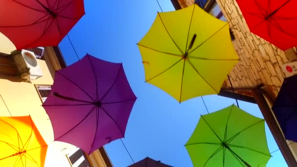 Opened, colorful, bold colored umbrellas, hanging from wires above the street. - Video