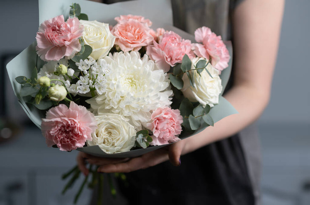 Close-up flowers in hand. Florist workplace. Woman arranging a bouquet with roses, chrysanthemum, carnation and other flowers. A teacher of floristry in master classes or courses - 写真・画像
