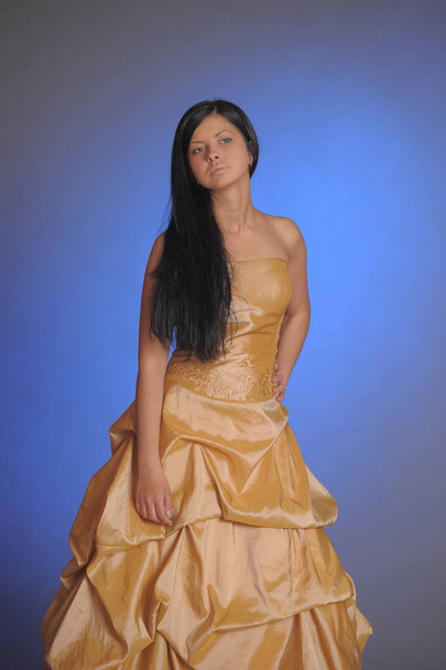 brunette girl in a long golden dress in the studio - Φωτογραφία, εικόνα