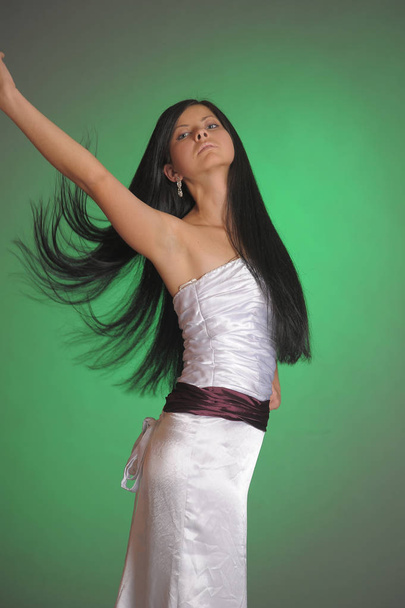 brunette girl in a long white dress in the studio on a green bac - Φωτογραφία, εικόνα