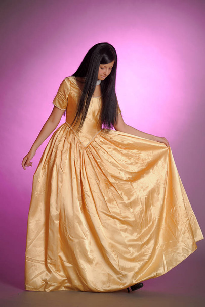 brunette girl in a long golden dress in the studio - Foto, imagen