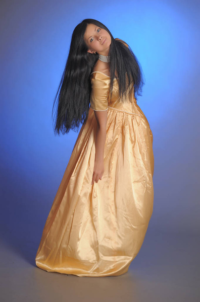 brunette girl in a long golden dress in the studio - Fotografie, Obrázek