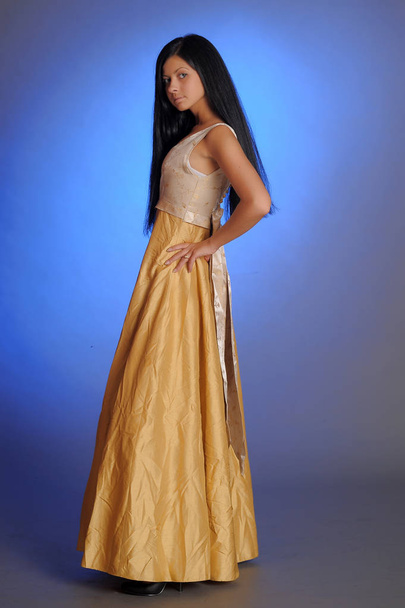 brunette girl in a long golden dress in the studio - Foto, afbeelding