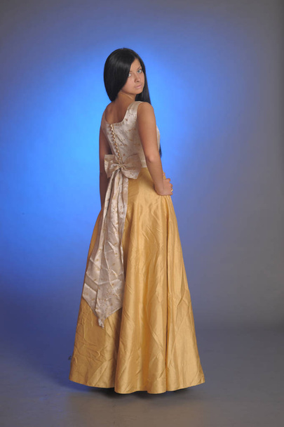 brunette girl in a long golden dress in the studio - Foto, imagen