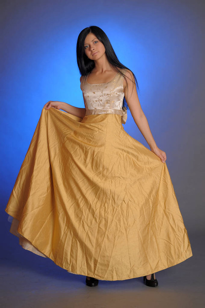 brunette girl in a long golden dress in the studio - Foto, afbeelding